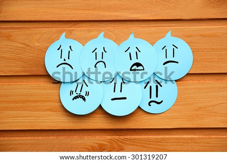 Sad emotions on blue stickers on wooden background. Group of negative emotions