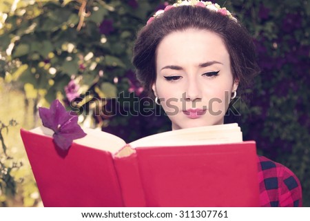 Portrait of beautiful young girl with the red book in the green garden.  Student. Thirst for knowledge. Dreaming woman. Reading book. Ukrainian girl