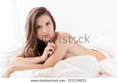 beautiful naked woman lying in bed and covering herself with white sheet