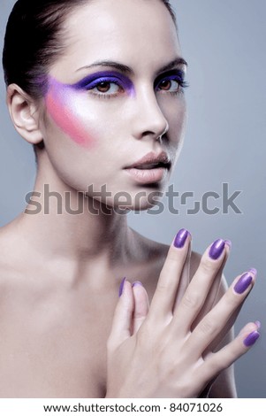 Portrait of attractive young woman with colorful makeup on face and painted finger nails; studio background.