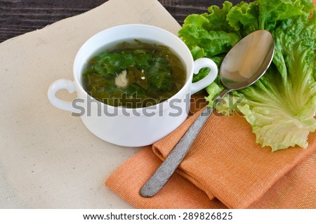 Hot or cold soup of green vegetables, chicken breast, eggs. A cup of soup on a green napkin orange.