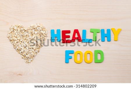 oat flakes in a heart shape on a wooden background. inscription colored letters healthy food