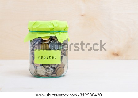 Financial concept. Coins in glass money jar with capital label. Wooden background
