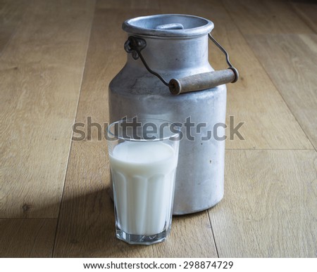 An old milk metal bottle and a glass of milk on a wooden table. These milk cans were common use in rural life until the Fifties in Italy.