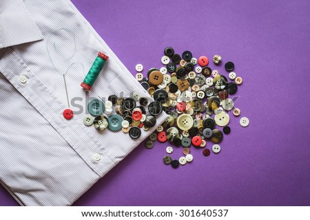 A handful of multicolor buttons, yarn and needle come to the aid of a shirt with a missing button. A red button not only fixes the problem but also breaks the rules bringing color to a boring shirt.