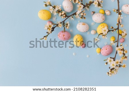 Happy Easter! Colorful Easter chocolate eggs with cherry blossoms flat lay on blue background. Stylish tender spring template with space for text. Greeting card or banner 商業照片 © 
