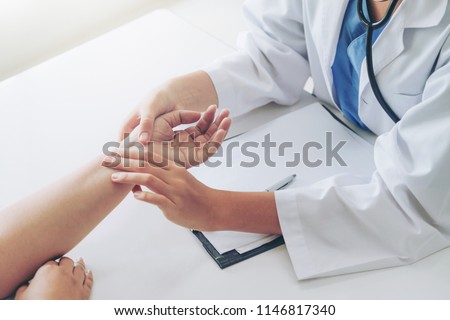 Woman doctor talks to female patient in hospital office while examining the patients pulse by hands. Healthcare and medical service. Stock fotó © 