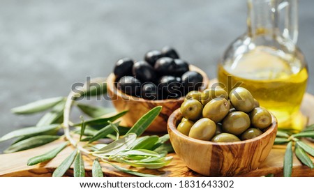 Set of green and black olives and olive oil on gray background. Different types of olives in olive wooden bowls and olive oil over wooden cutting board and olive leaves. Copy space. Horizontal banner