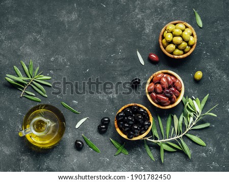 Set of green, black and red or pink olives and olive oil on dark background. Different types of olives in olive wooden bowls and olive oil over dark canvas background. Copy space. Top view or flat lay