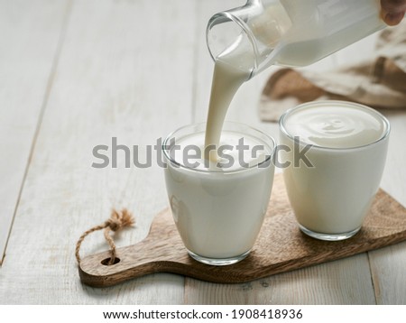 Pouring homemade kefir, buttermilk or yogurt with probiotics. Yogurt flowing from glass bottle on white wooden background. Probiotic cold fermented dairy drink. Trendy food and drink. Copy space left Сток-фото © 