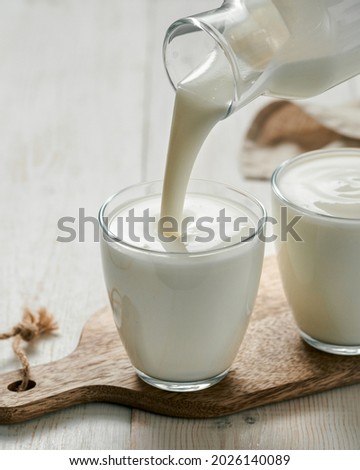 Pouring kefir, buttermilk or yogurt with probiotics. Yogurt flowing from glass bottle on white wooden background. Probiotic cold fermented dairy milk drink. Vertical Сток-фото © 