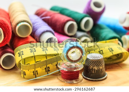 heap of sewing color bobbins threads, measure tape and old thimble on wooden table with blur background