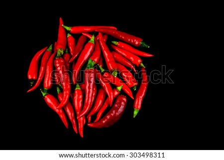 A stack of fresh small fiery red chillis isolated against a black background