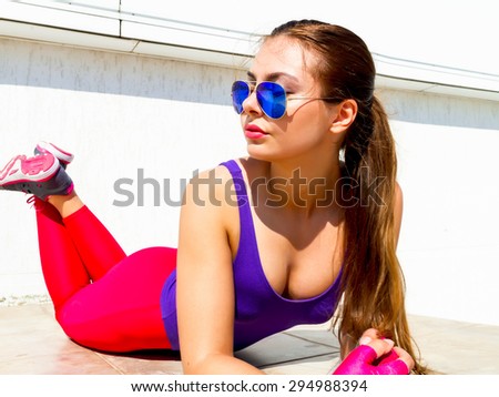 Summer Close-up fashion portrait sexy sportive woman with tan skin,pink big lips and long brunette hair wearing violet swimsuit pink leggins, glasses  relaxing and takes the sun after yoga  training.
