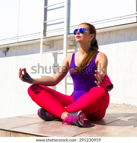 Yoga woman meditating at sunrise. Female model meditating in serene harmony in lotus position. Healthy wellness lifestyle with multicultural young woman.wearing violet swimsuit,pink leggins, glasses