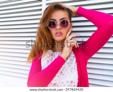 Fashion portrait of pretty young hipster blonde woman with bright sexy make up and glasses, wearing stylish pink t shirt. White urban wall background. Summer Trendy fashion concept.