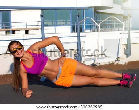 Strong attractive sportive woman with tan skin and long brunette hair doing side plank exercise on outdoor roof. Fit doing side plank.fitness and diet concept - smiling teenage girl doing side plank