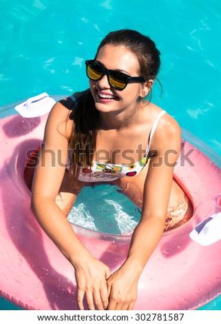Beautiful sexy young woman with perfect slim figure with long dark hair and wet bathing suit fashion in stylish glasses.Happy Glamour girl with pink inflatable circle in Pool. Party Summer Style.