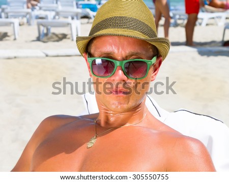 Sexy hot muscular Man on beach looking to camera ,wearing hipster hat, sunglasses.Young man enjoying summer travel holiday by the ocean on luxury beach resort.Portrait of a man staring at the camera.