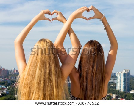 Teenage sisters holding hands together.Two female friends holding hands up in summer.Two young woman making heart shape with hands.Two young girl friends standing together,having fun.Amazing city view