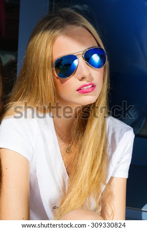 Close up fashion portrait of young blonde woman. Close up fashion portrait of pretty hipster woman with long blonde hairs, wearing stylish trendy blue sunglasses, bright colors. Wind,morning.