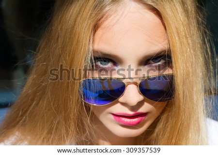 Summer Close up fashion portrait of young blonde woman. Portrait of pretty hipster woman with long blonde hairs, wearing stylish trendy blue sunglasses, bright colors. Bright make up.Looking to camera