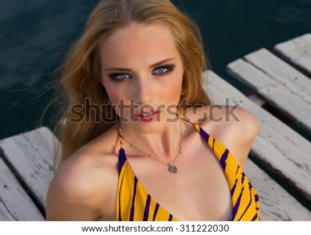 Summer close up fashion portrait of young woman, calm emotions,on sea pier.Glamour portrait of beautiful woman model with bright makeup and romantic wavy hairstyle.Sunset time,toned colors.