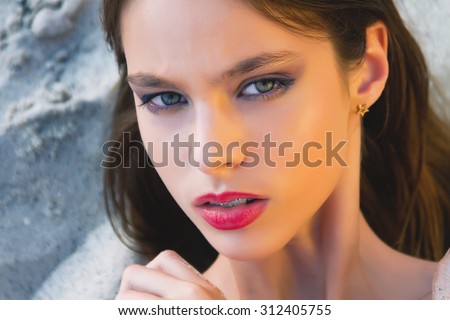 Summer close up fashion portrait of brunette young woman, calm emotions,on sea beach.Glamour portrait of beautiful woman model with bright makeup and romantic wavy hairstyle.Sunset time,toned colors.