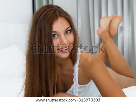 Morning portrait of  pretty woman with green eyes,sensual happy face,positive emotions,laying in bed in white bedroom.Pretty lingerie.Perfect sexy tan woman with perfect skin, big full lips,long hair