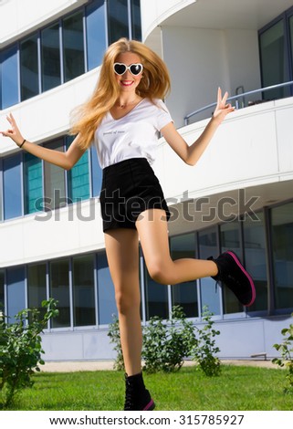 Summer fashion full lenght of Young Excited Girl Jumping.Hipster girl jumping and scramming on the street,wearing short black shorts,boots, white t-shirt.Young blonde woman going crazy and having fun