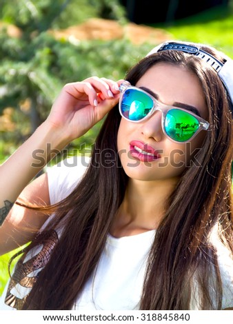 Trendy Hipster Girl Relaxing on the Grass.Modern Youth Lifestyle Concept.happy  brunette girl walking in the green summer park,enjoy sunny day and summer vacation. smiling looking at camera.