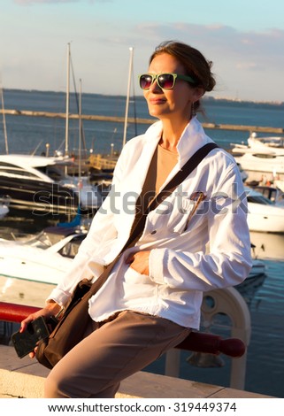 Mature pretty woman wearing white jacket and beige clothes,enjoying a relaxed sunny day out at a marina, with boats as background, with blue sky as copy space.Beautiful sunset at the yacht club