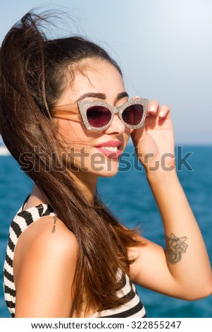 Summer fashion close up portrait of young woman looking to the ocean,enjoy her freedom and fresh air,wearing striped dress and vintage sunglasses at sea background.Beautiful girl  at summer beach.