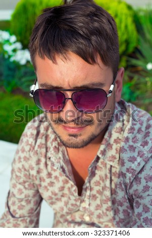 Outdoor close up portrait  of stylish man wearing casual shirt and sunglasses at urban bright background.Hipster man portrait looking aside in a park.Man has beard and he is outdoor.