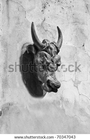 A bulls head sculpture on a cracked and rustic wall in black and white