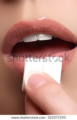 Closeup detail of woman putting pink chewing gum into her mouth. Chewing Gum, Eating, Women. Close up on a beautiful girl while enjoying a candy.