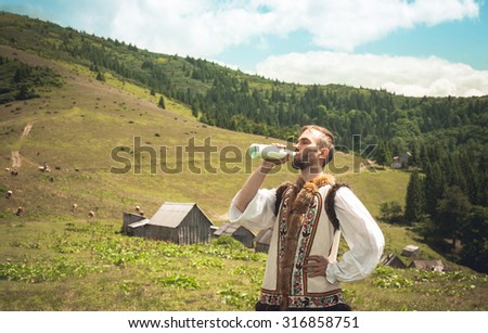 young man wearing traditional clothes drinking milk on a background of mountains