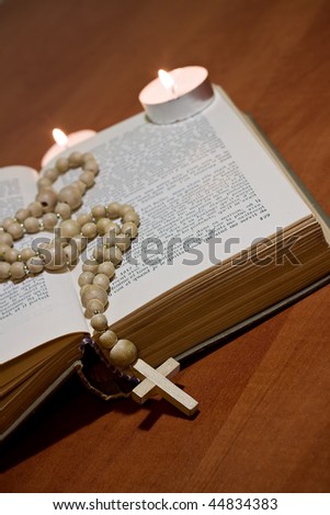 Old Cross and the Holy Bible laying on the table in front of a lighting candle.