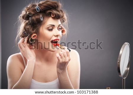 Portrait of a young woman with long hair on gray background making beauty face and hair style. Smile happy girl seating at table with make up accessories and mirror, creating home beauty salon
