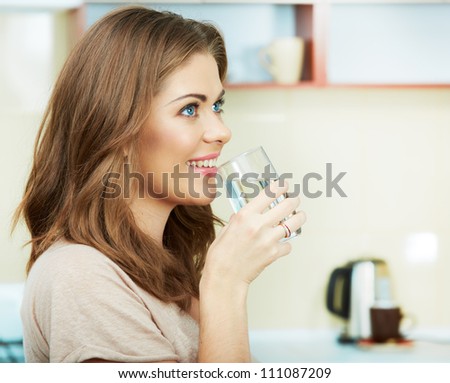 Portrait of happy  young woman drinking water against kitchen background.