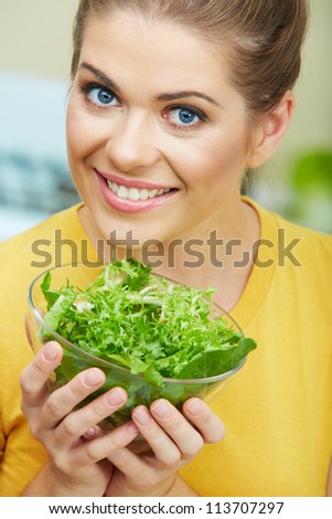 Woman with vegetarian food  standing against  home kitchen interior eating healthy food. Yellow color clothes. Close up woman face portrait.