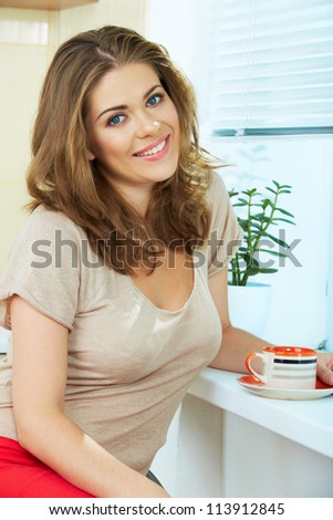 Portrait of dreaming  woman  holding coffee cup sitting near a window at the kitchen interior. Close up smiling female face.