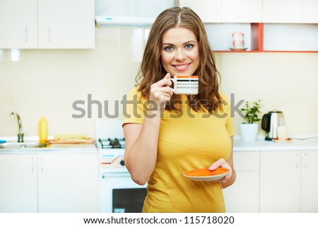 Portrait of young smiling woman holds a cup with coffee or tea against kitchen background. Yellow color clothes.