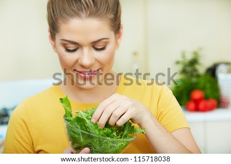 Happy Woman eating  vegetarian food,  standing against  home kitchen interior background. Yellow color clothes. Woman Face close up portrait.