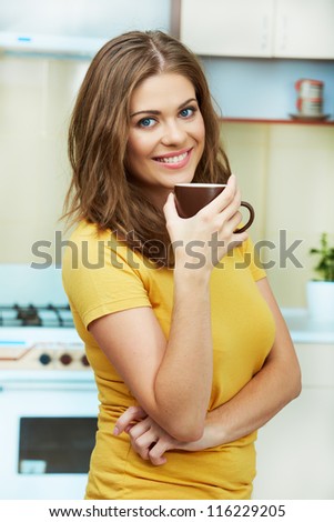 Portrait of young woman holds a cup with coffee or tea against kitchen background.