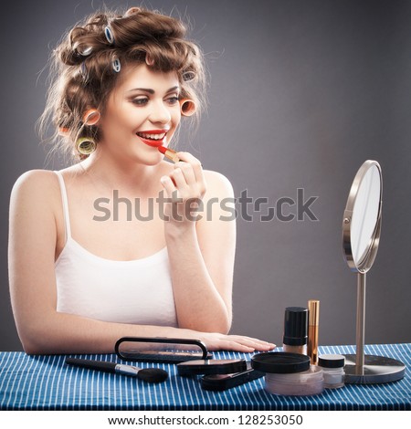Portrait of a young woman with long hair on gray background making beauty face and hair style. Smile happy girl seating at table with make up accessories and mirror, creating home beauty salon