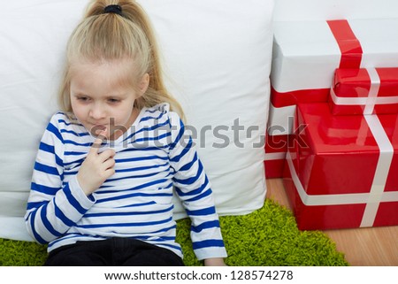 Thinking little girl with white hair and many gifts . Seat on floor.