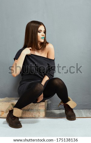 Fashion model with straight hair. Young beautiful woman seat against wall.