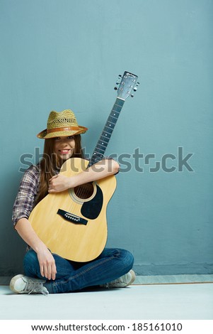 Teenager girl seating on a floor with acoustic guitar.