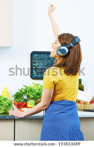 Woman standing back in kitchen, cooking healthy food with fun and listen music with headphones.